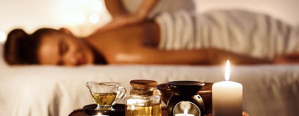 mani che massaggiano la schiena di una donna in primo piano oli essenziali e candela