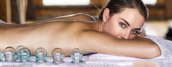 una donna che ti guarda distesa su un lettino benessere con coppette in primo piano
